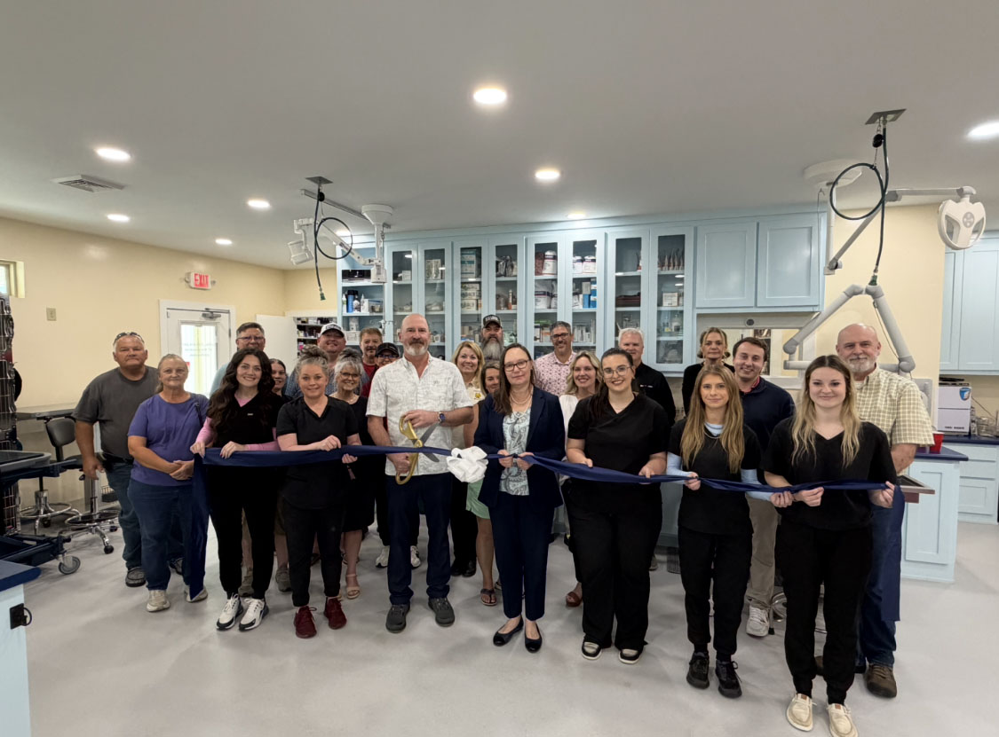 group of people smiling during a ribbon-cutting ceremony inside a veterinary clinic blue cabinets medical equipment in the background